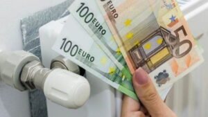 ένα χέρι κρατά 2 χαρτονομίσματα των 100 ευρώ και ένα των 50 μπροστά από ένα σώμα καλοριφέρ