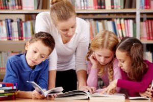 Μια δασκάλα βοηθάει τρία καθισμένα παιδιά στο διάβασμα