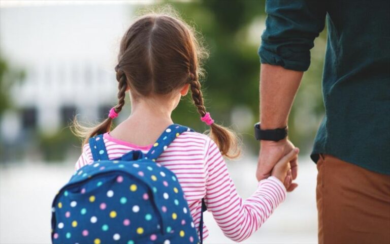 Κοριτσάκι με μπλε σχολική τσάντα πάει στο σχολείο κρατώντας το χέρι ενός άνδρα