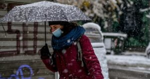 Αλλάζει ο καιρός από την Κυριακή 7/1: Στη φωτογραφία πολίτης με κόκκινο μπουφάν και μαύρο σετ γάντια - κασκόλ κρατάει ομπρέλα εν μέσω χιονιά