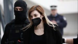 Κατηγορούμενη Ρούλα Πισπιρίγκου με μαύρη μάσκα και μαύρα ρούχα, συνοδευόμενοι από αστυνομικούς