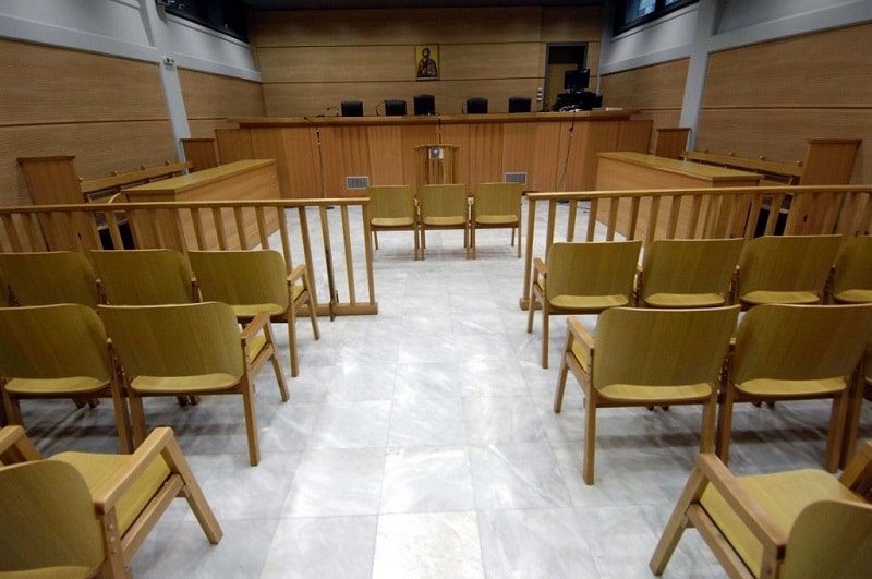 Αίθουσα δικαστηρίου με καρέκλες δεξιά και αριστερά διάδρομο στη μέση και έδρανο δικαστών