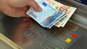 ένα χέρι κρατά χαρτονομίσματα των 50 και 20 ευρώ μπροστά από ένα μηχάνημα ΑΤΜ