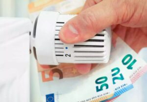 ένα χέρι ρυθμίζει τον θερμοστάτη καλοριφέρ ενώ ταυτόχρονα κρατά χαρτονομίσματα των 10, 20 και 50 ευρώ