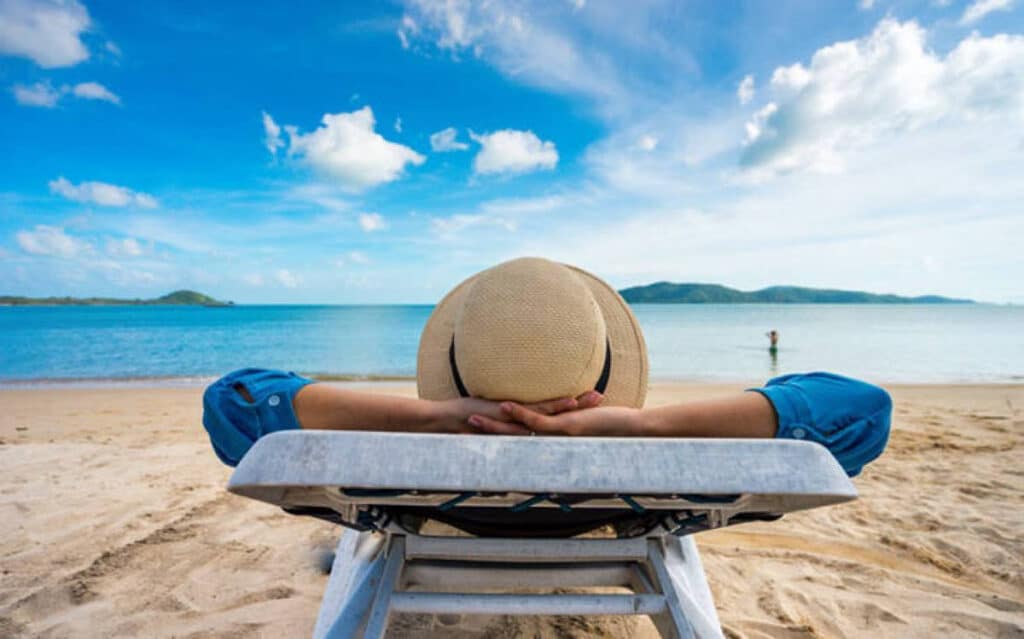 γυναίκα ξαπλωμένη σε ξαπλώστρα φορώντας καπέλο αγναντεύει τη θάλασσα. Τουρισμός