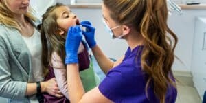 μητέρα κρατά το κοριτσάκι της την ώρα που το εξετάζει η οδοντίατρος
