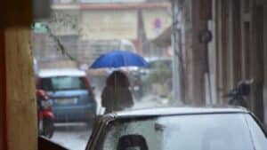 Γυναίκα στον δρόμο εν ώρα βροχής που κρατάει μπλε ομπρέλα
