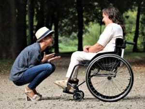 μια γυναίκα σε αναπηρικό καροτσάκι κουβεντιάζει με την προσωπική της βοηθό σε πάρκο