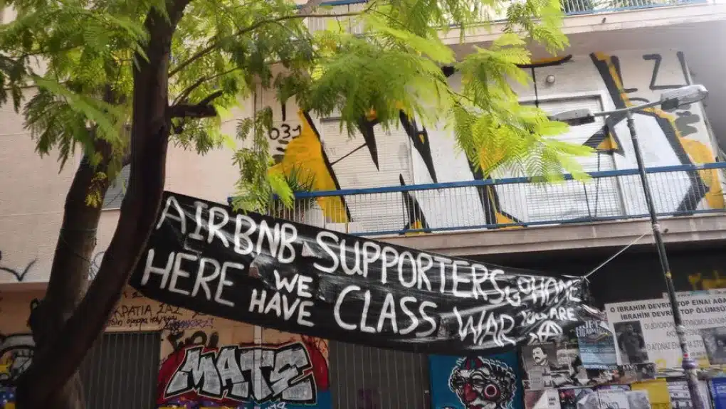 Διαμαρτυρία κατά του Airbnb στα Εξάρχεια, Ελλάδα. Υψωμένο πανό με σύνθημα στα αγγλικά
