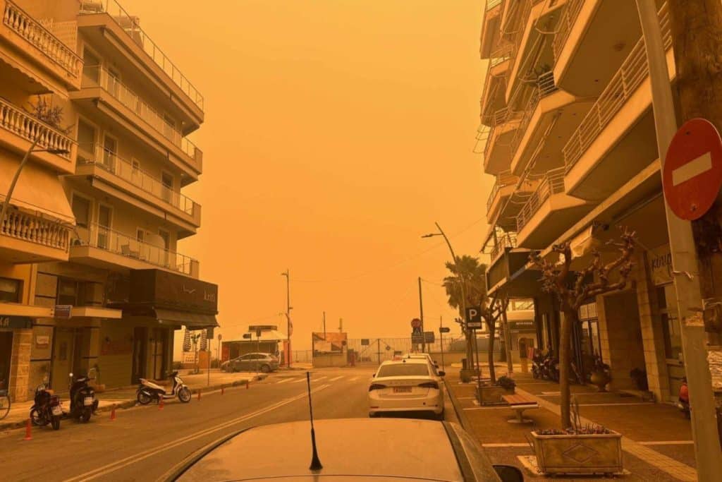 Αφρικανική σκόνη: Πορτοκαλί ατμόσφαιρα σε δρόμο της Αθήνας με πολυκατοικίες δεξαιά και αριστερά.
