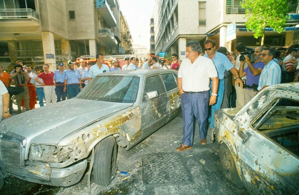 Ο Γιάννης Παλαιοκρασσάς εξετάζει τα κατεστραμμένα αυτοκίνητα μετά την επίθεση της «17 Νοέμβρη» στο κέντρο της Αθήνας, στις 14 Ιουλίου 1992\.
Πηγή φωτογραφίας\: Φωτογραφία αρχείου